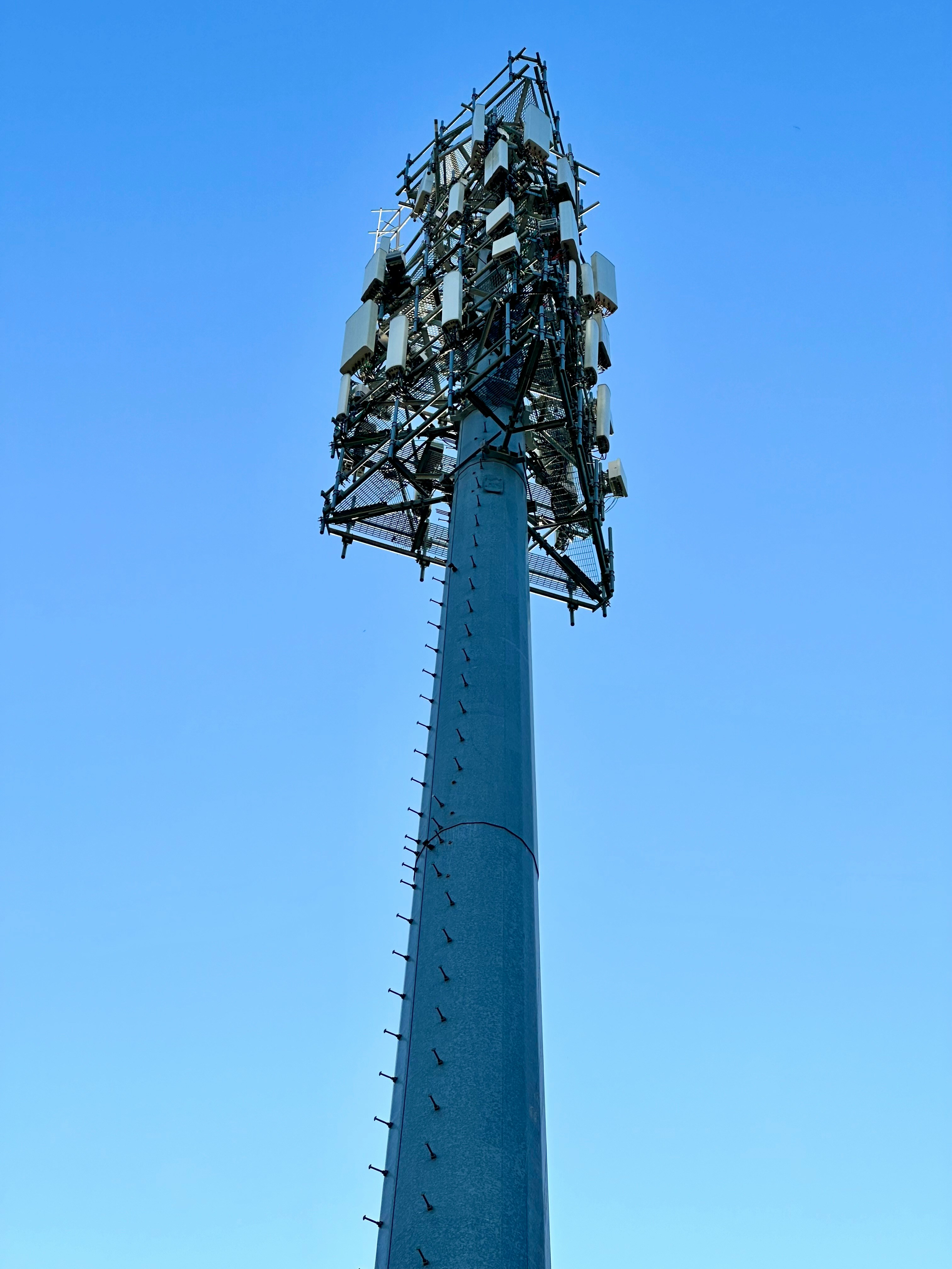 A heavily loaded monopole tower packed with antenna hardware against a blue sky